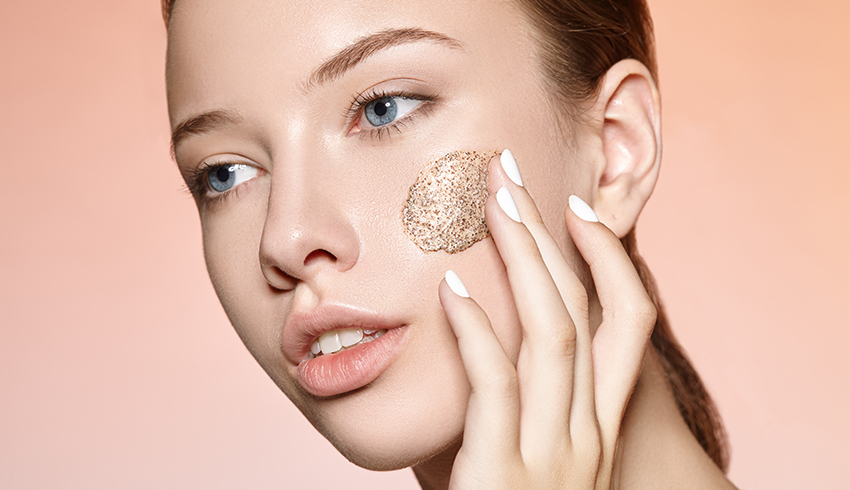 A woman applies an exfoliant to her cheek